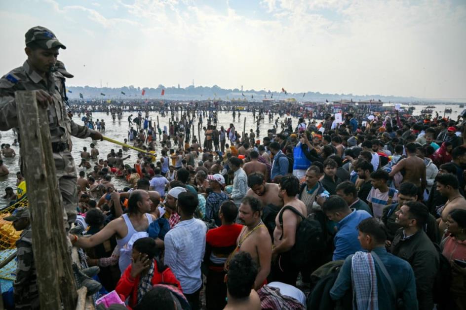 A large crowd stands near a large river, with some people in the river.