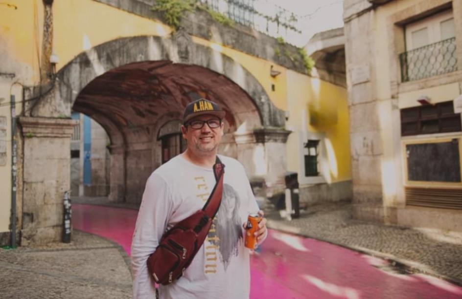 A man with a canned drink in his hand standing near a colourful road and an overpass