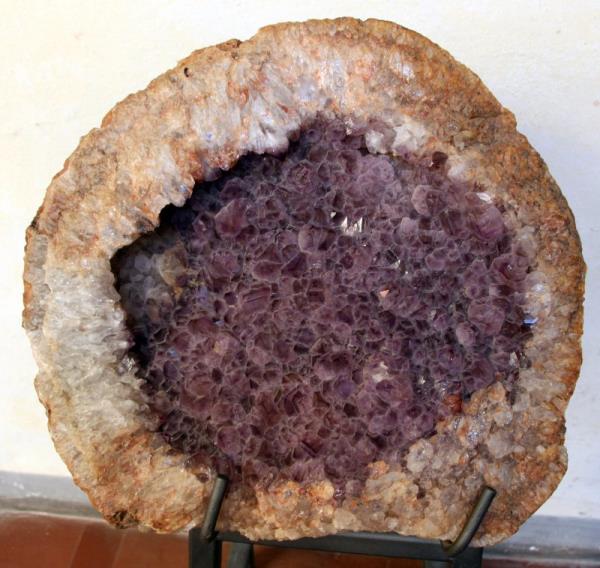 Broken-open spherical rock with thick brown outer layer closely lined with small purple crystals within.