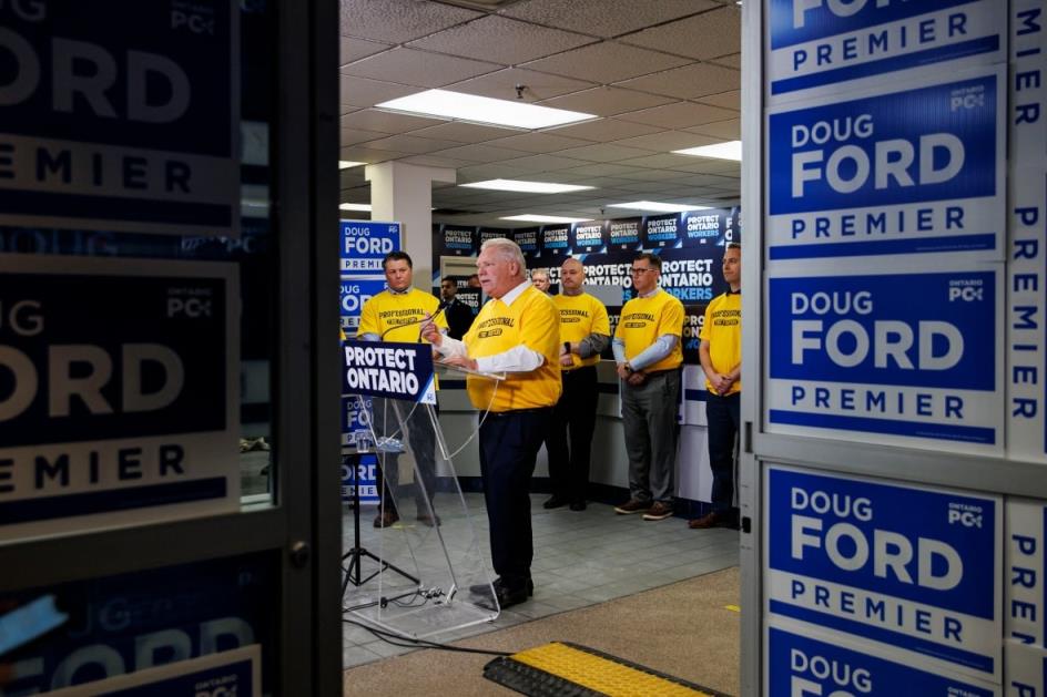 Doug Ford wears a yellow t-shirt, standing at a podium that says 'Protect Ontario.