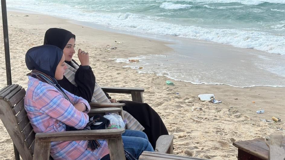 Two women sit by the shore.