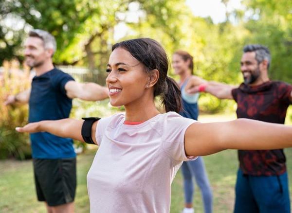 Group of multiethnic mature people stretching arms outdoor. Middle aged yoga class doing breathing exercise at park. Beautifil women and fit men doing breath exercise together with outstretched arms. 