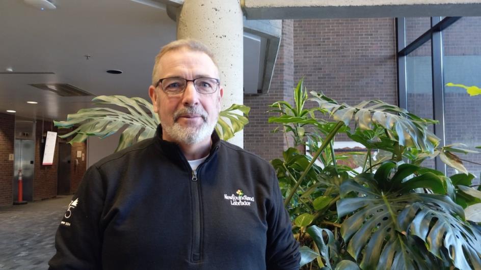 Man in black sweater standing in front of green plant.