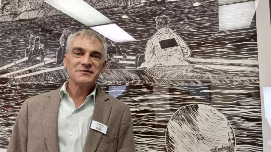 Man in grey suit standing against a black and white drawing.