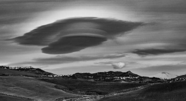 Cloud shapes: Black-and-white view of flying saucer shaped clouds over over a mountainous landscape.