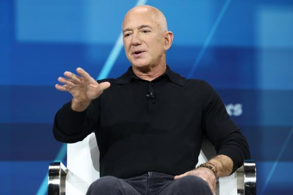 Jeff Bezos speaking at the New York Times DealBook summit, December 04, 2024 with his arm outstretched.